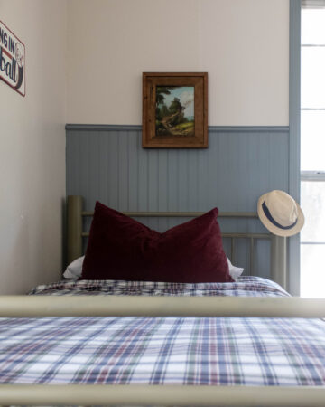 blue beadboard accent wall with dark red pillow on plaid bed